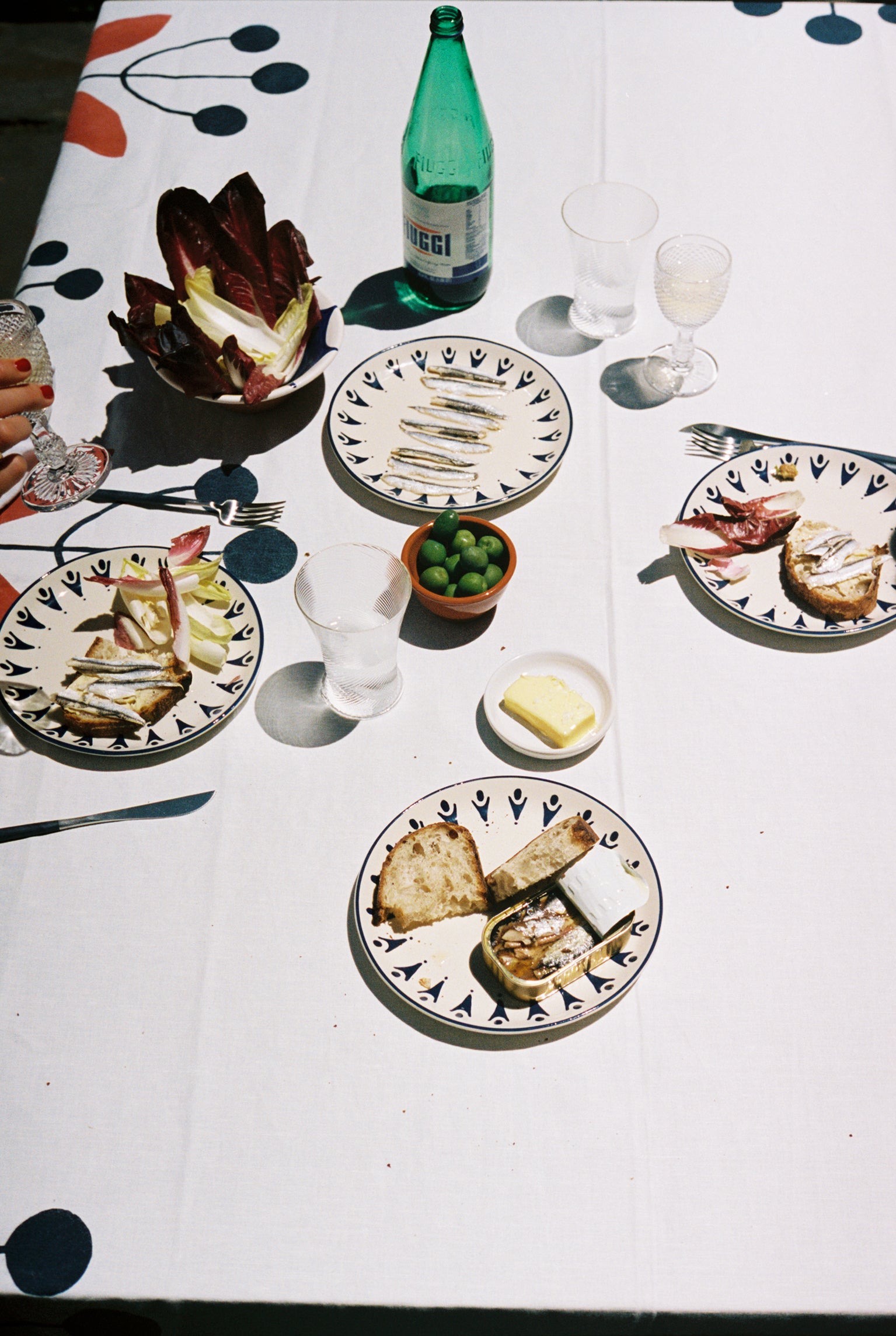 Tablescape on white cloth with Vito Dinner Plates, bread, tinned fish, and olives.
