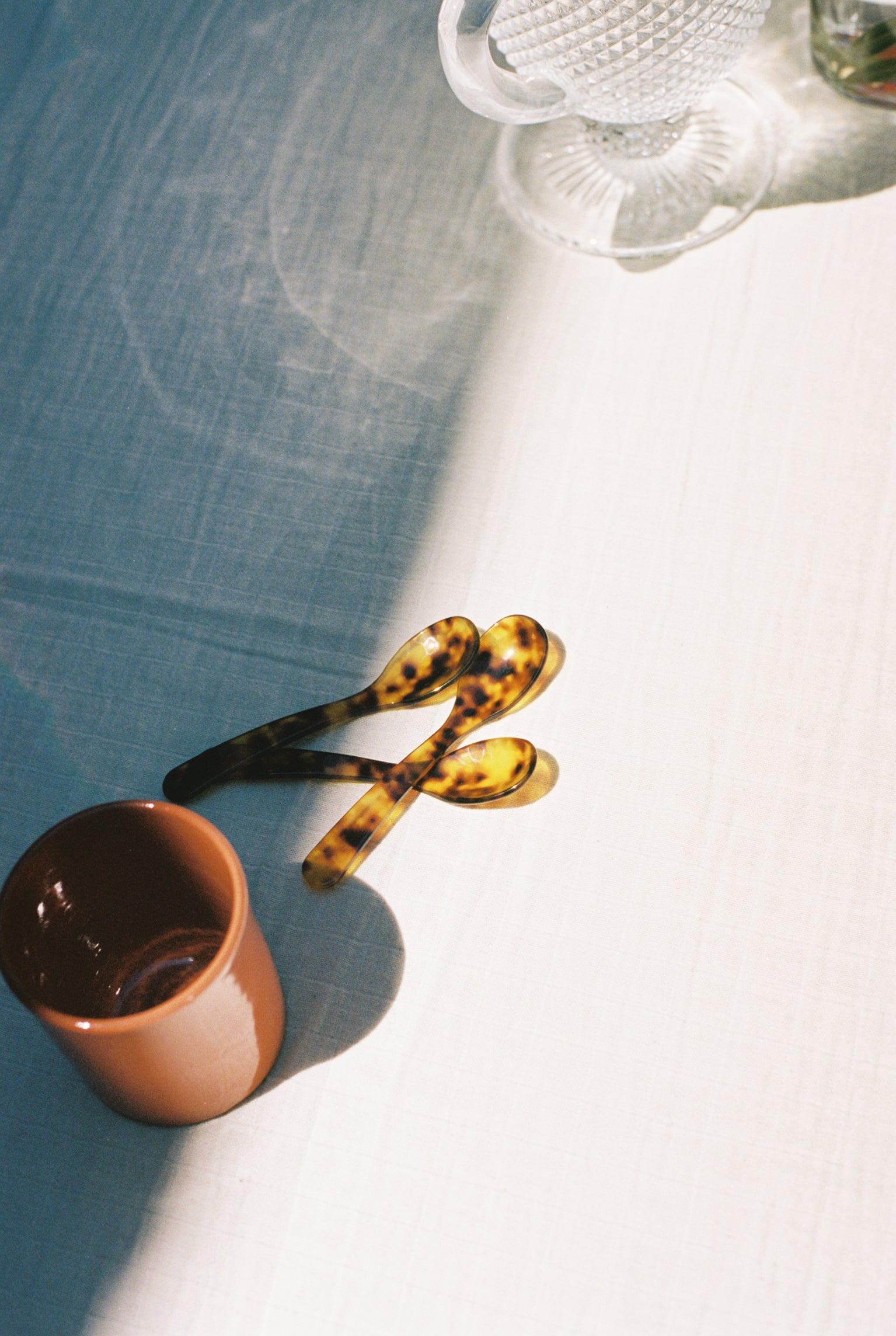 Group of Piccolo Spoons on white tablecloth near terracotta mug.