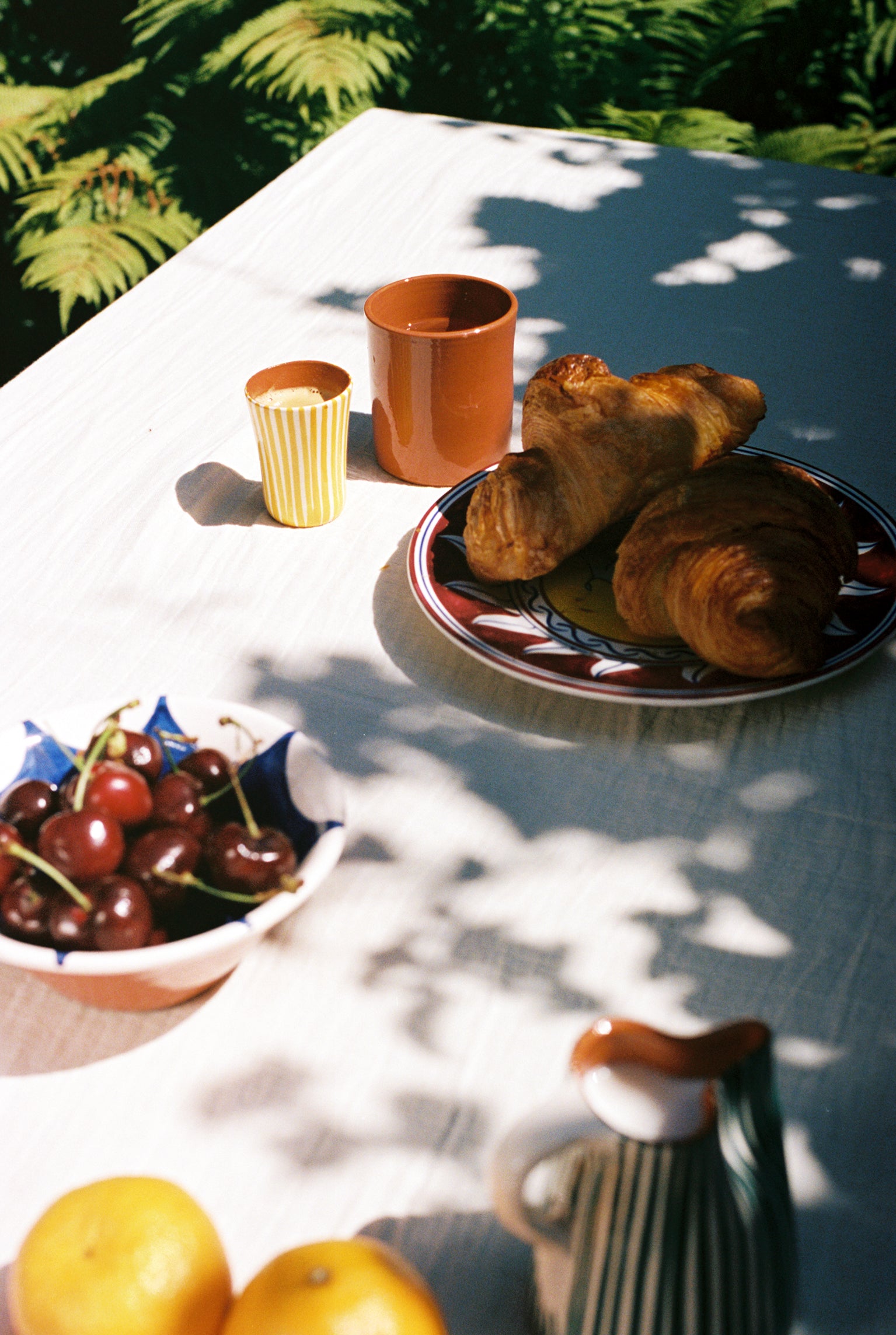 Yellow espresso cup on outdoor tablescape with croissants and cherries.