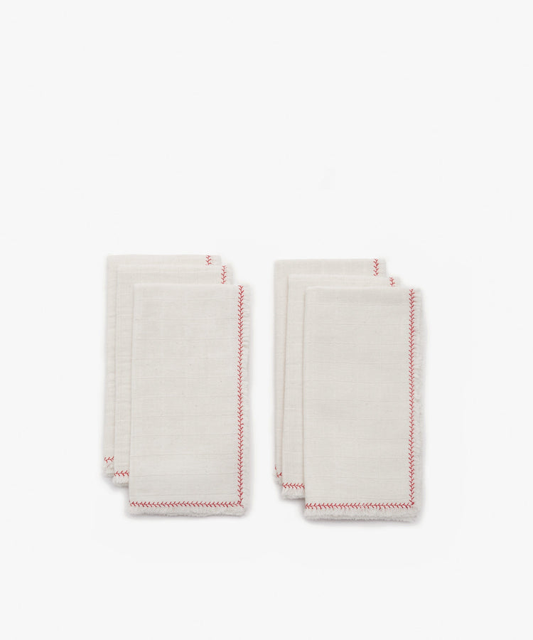 Six neatly folded Filial Napkin sets, in white cotton with red stitched edges, arranged in two pairs on a plain white tabletop.
