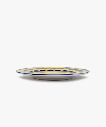 Palio Dinner Plate. Glazed ceramic in yellow and navy designs with tortoise motif, angled side view.