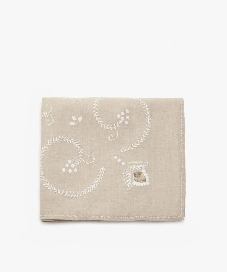 Inez Tablecloth. Folded cloth in tan cotton with white embroidered floral motif.