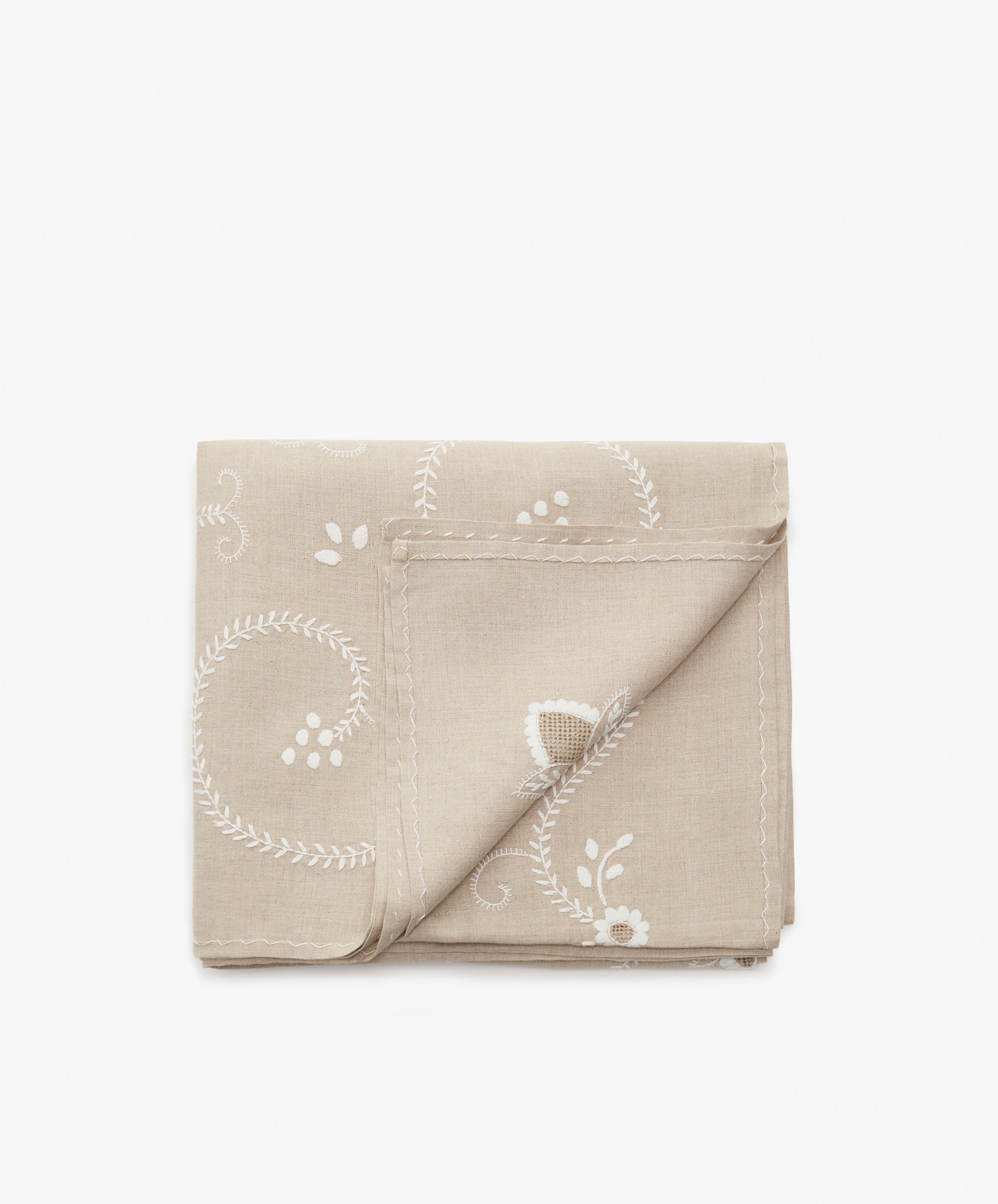 Inez Tablecloth in tan cotton and white embroidery, folded with corner flipped up.