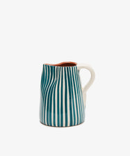 The Natalia Milk Jug is a handmade piece with blue vertical stripes and a white handle, adding charm to any breakfast table.