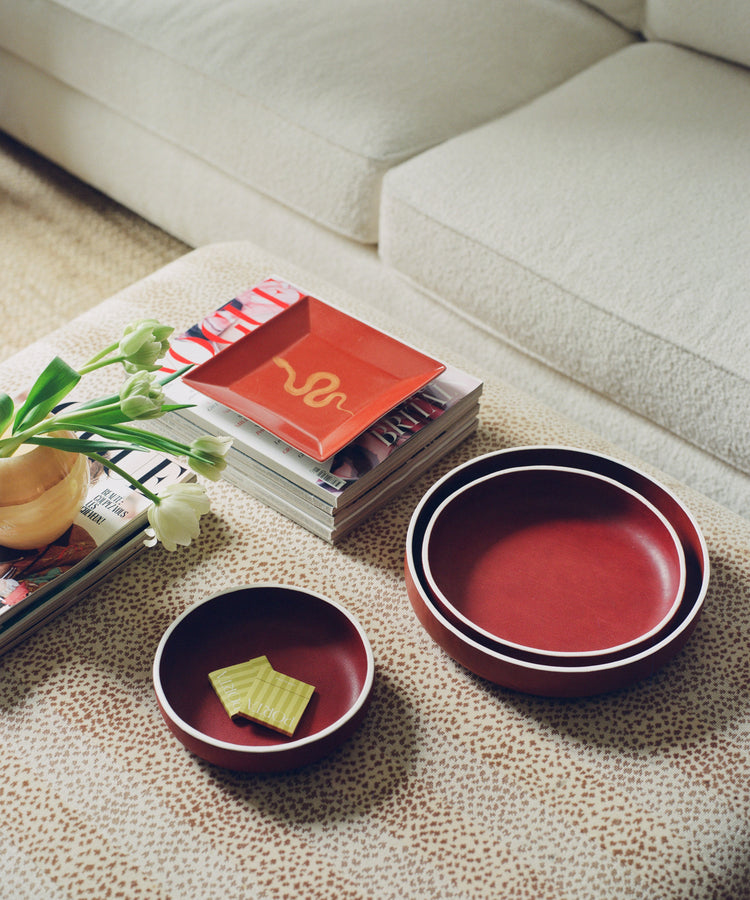 Two red ceramic bowls on a patterned table with a book stack and flowers nearby.