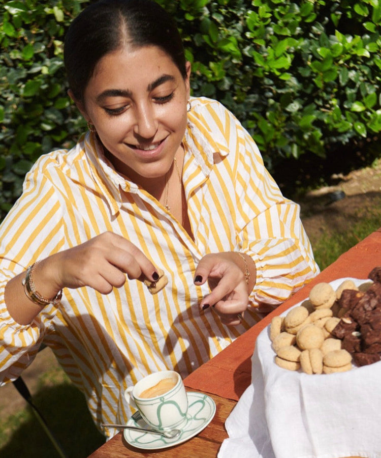 Woman dipping a cookie into a cup of coffee at an outdoor table with a basket of cookies