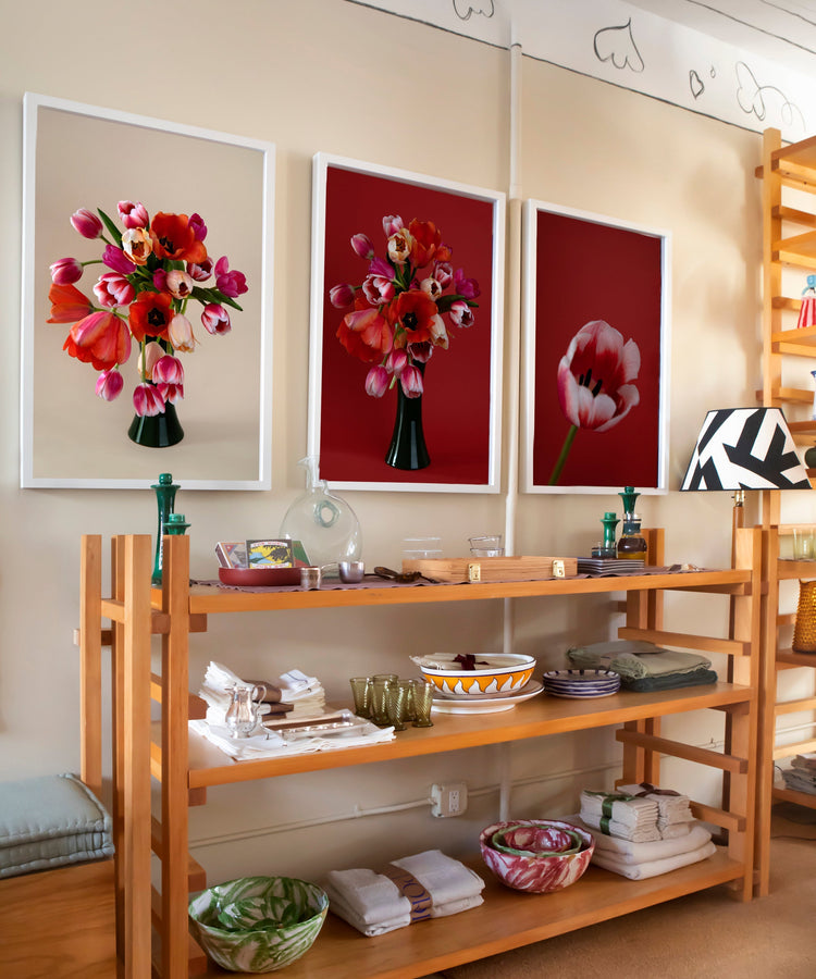 ChatGPT said:  Wooden shelving unit with bowls, plates, and folded linens, set against a wall with three framed floral prints in red tones.