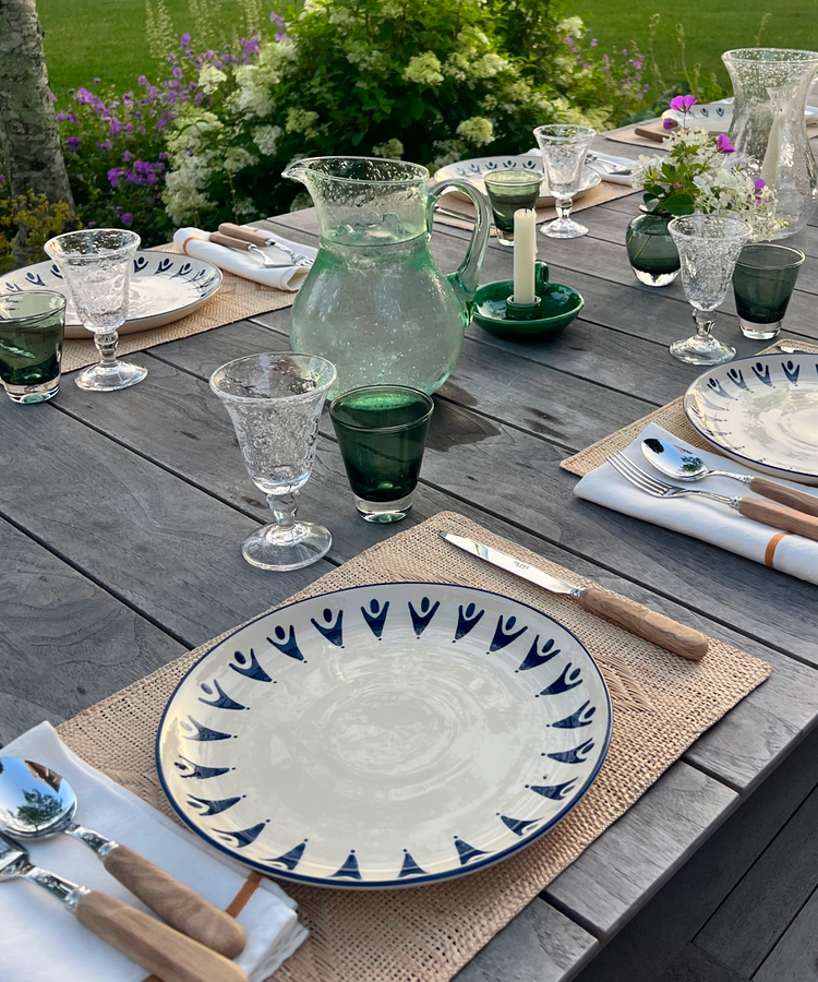 Elegant outdoor table setting with patterned plates, green glassware, and fresh flowers.