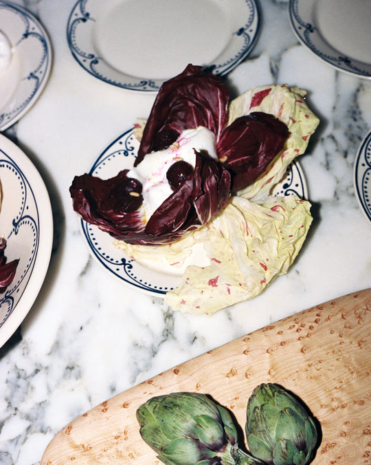 Artichoke dish with whipped cream on a marble surface with plates in the background
