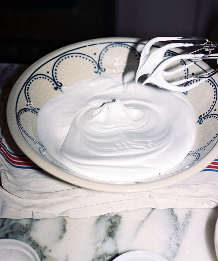 The handmade Arco Serving Bowl holds thick, glossy whipped egg whites on a kitchen counter, as a beater lifts out stiff peaks.