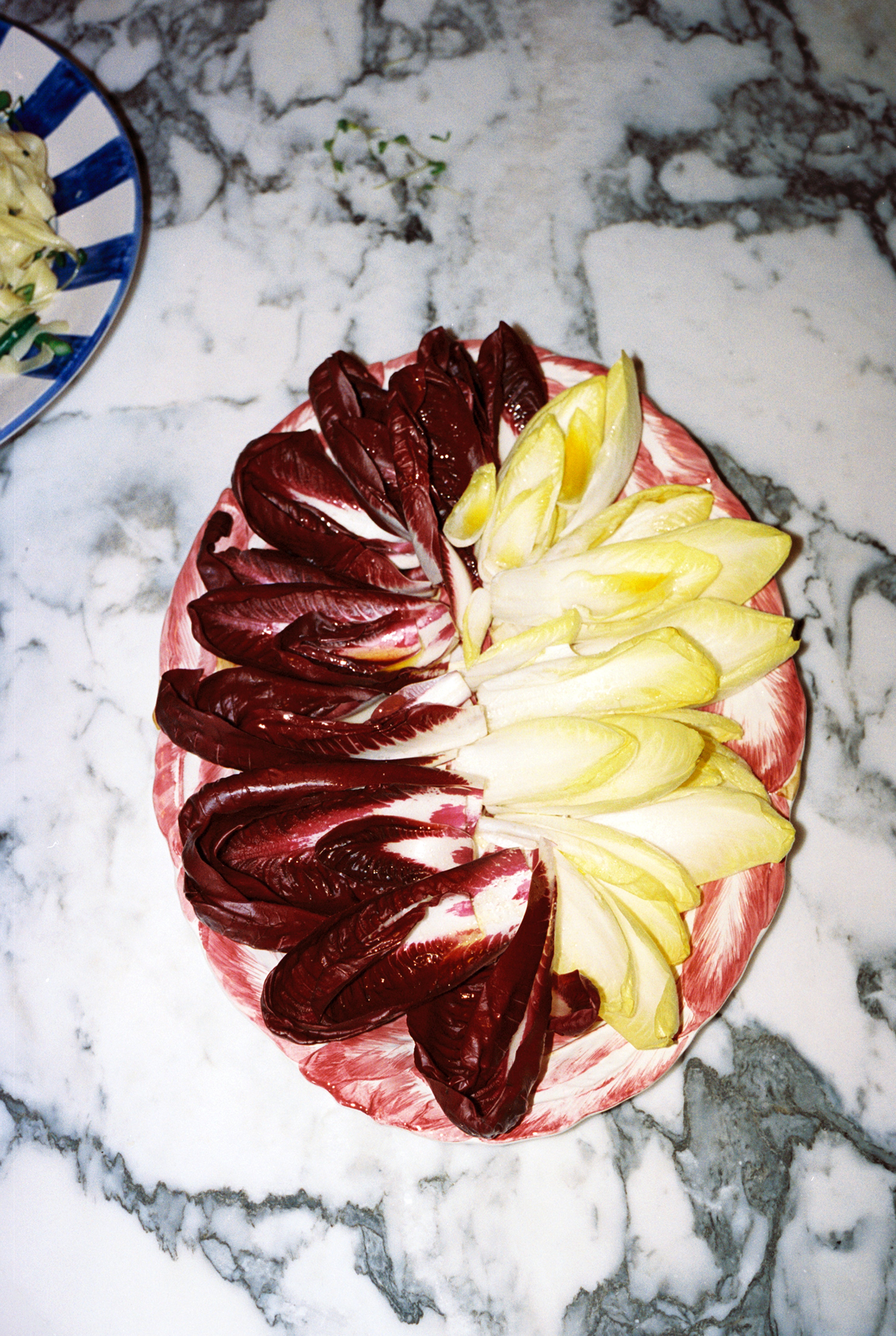 A plate with arranged red and yellow endive leaves sits on a marble countertop; at the top left is a partially visible Radicchio Oval Serving Platter.