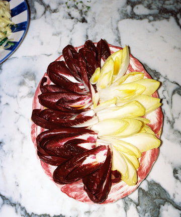 A plate with arranged red and yellow endive leaves sits on a marble countertop; at the top left is a partially visible Radicchio Oval Serving Platter.
