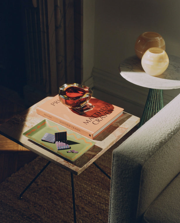 Small side table with books, a red glass bowl, and a green tray holding matchboxes.