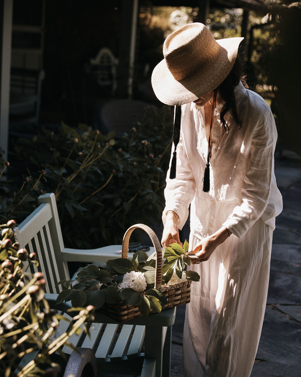Wearing the Wosto Hat and light clothing, a person arranges flowers in a basket outdoors on a bench, staying protected from the sun while working.