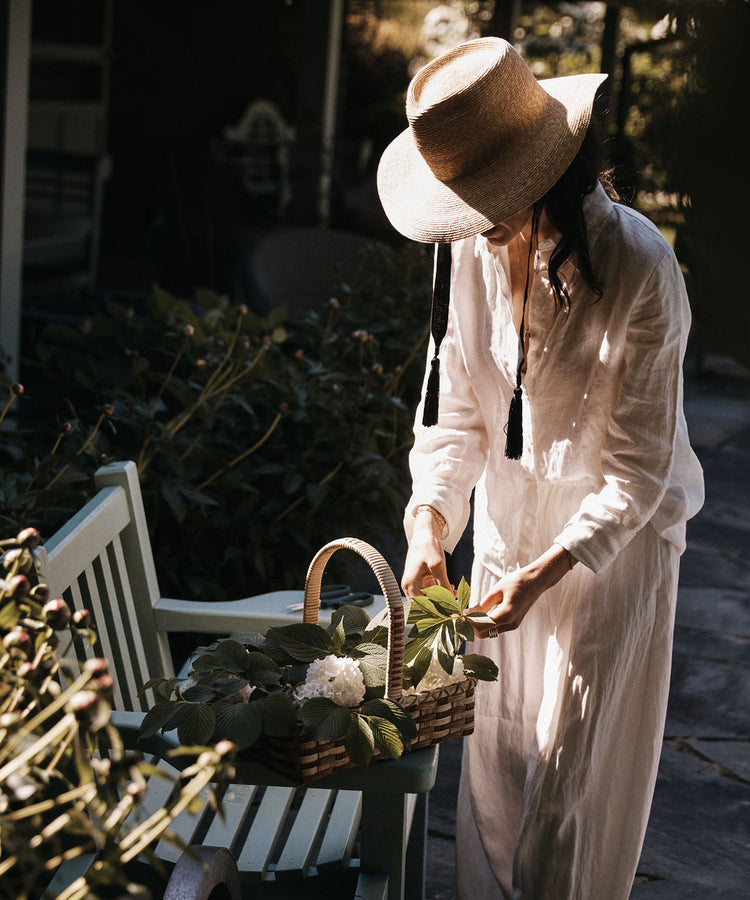 Wearing the Wosto Hat and light clothing, a person arranges flowers in a basket outdoors on a bench, staying protected from the sun while working.