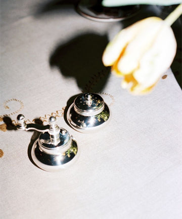 The Jules Pepper Mill and Salt Shaker rest on a light tablecloth, with a yellow tulip overhead casting a shadow—a subtle nod to refined Italian craftsmanship.