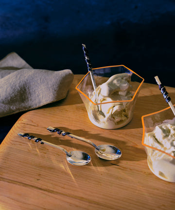 Set of silver ice cream spoons in situ on wood board and with ice cream from glass bowls.