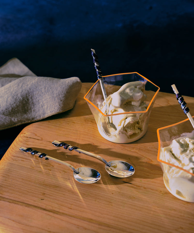 Set of silver ice cream spoons in situ on wood board and with ice cream from glass bowls.