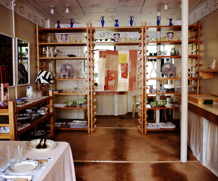 interior of store with wooden shelves of ceramics and hanging quilt 