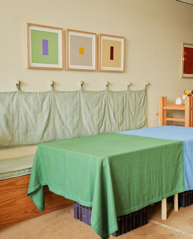 Room with two beds, green and blue covers, and three framed abstract artworks on the wall.