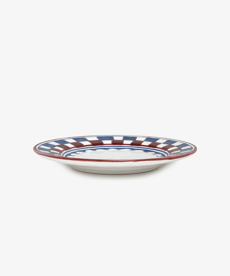 The Luca Small Plate, Set of 4, features a white ceramic base with hand-painted blue and red checkered and striped patterns around the rim, shown from a side view against a plain background.