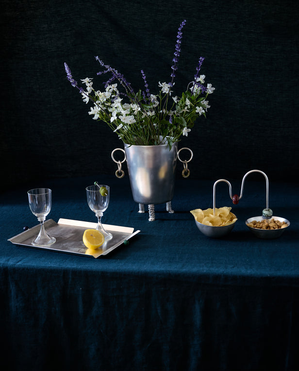 table with cocktail glasses on silver tray , silver bowl with chips and nuts and silver ice bucket with flowers