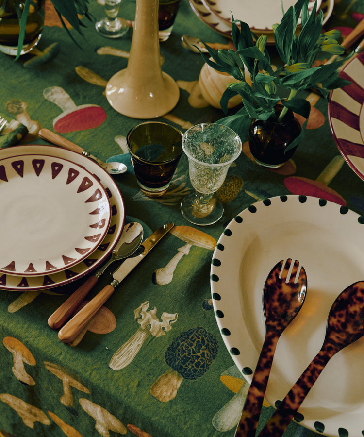 Table set with decorative plates, cutlery, green plants, and a green tablecloth featuring mushroom illustrations, complemented by the Gem Glass, Set of 2 luxury glassware.