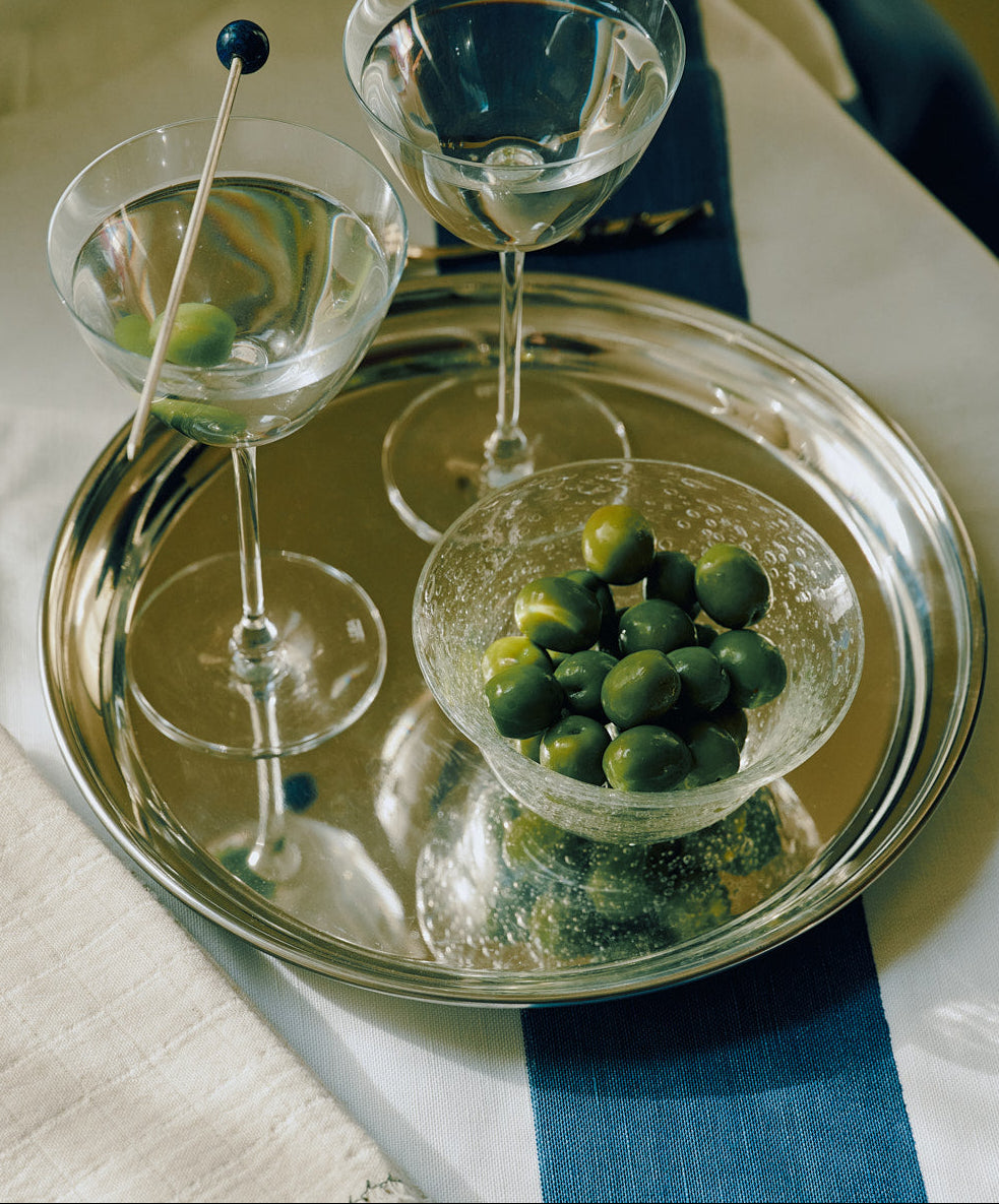Two martini glasses and a small bowl of green olives are arranged on the Sophie Tray atop a white and blue-striped tablecloth.