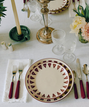 Table setting with Daria Small Plate, Set of 4, silverware with red handles, crystal glasses, a candlestick and candle, plus flowers on a white tablecloth—ideal for everyday use.