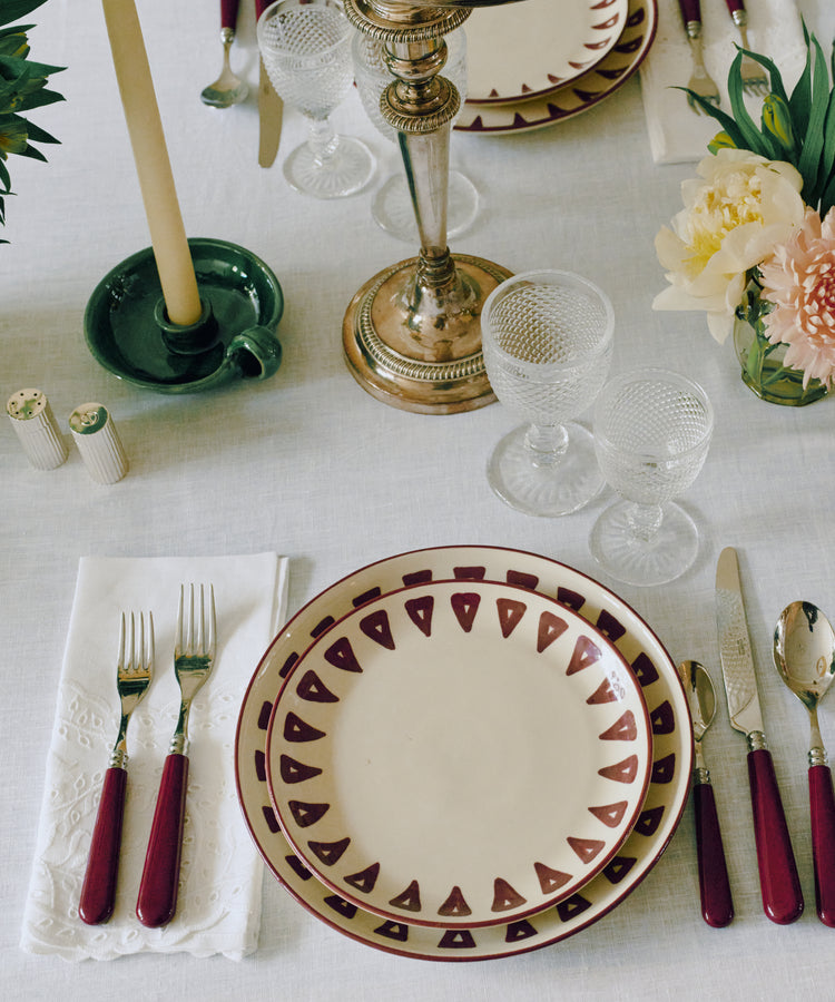 Table setting with Daria Small Plate, Set of 4, silverware with red handles, crystal glasses, a candlestick and candle, plus flowers on a white tablecloth—ideal for everyday use.