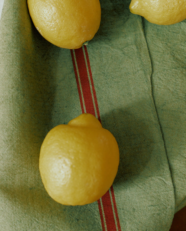Three lemons rest on a richly dyed green cloth with a red stripe, reminiscent of the French Vintage Tea Towel.