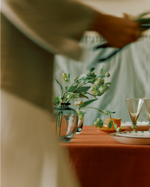 Dining table with floral arrangement, glasses, and plates with a blurred person in the foreground.