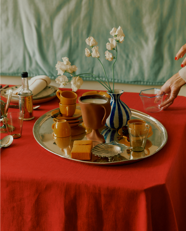 Table setting with a red tablecloth, silver tray, and decorative items.