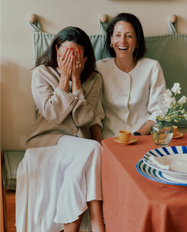 Two women sitting at a table with a floral arrangement and plates.