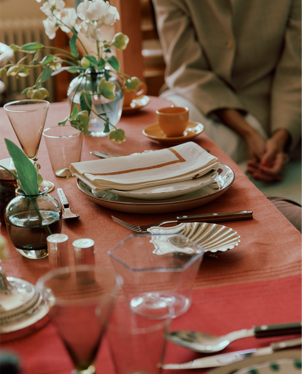 Dining table set with plates, glasses, and flowers with a person partially visible.