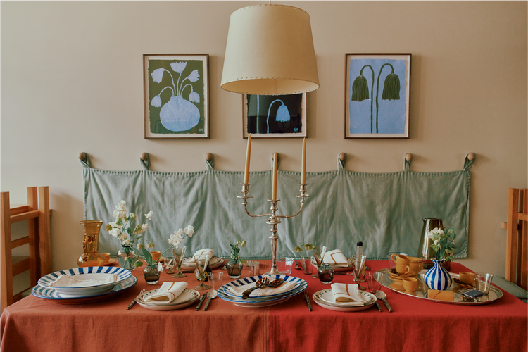 Dining table set with plates, glasses, and cutlery, with a red tablecloth and decorative elements.