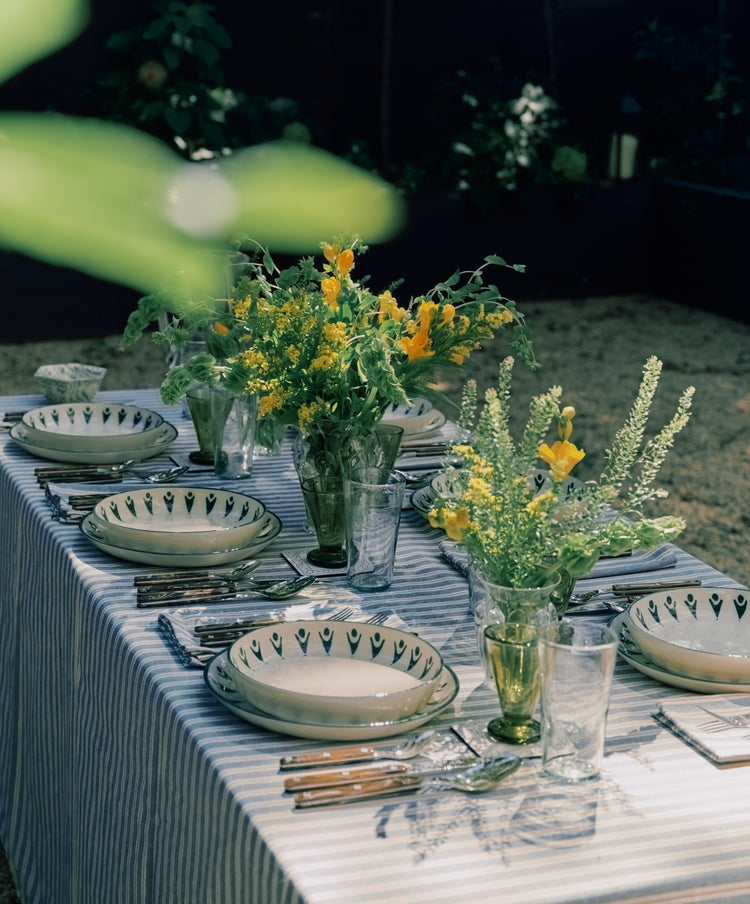 Dining table set with plates, glasses, and floral arrangements outdoors.