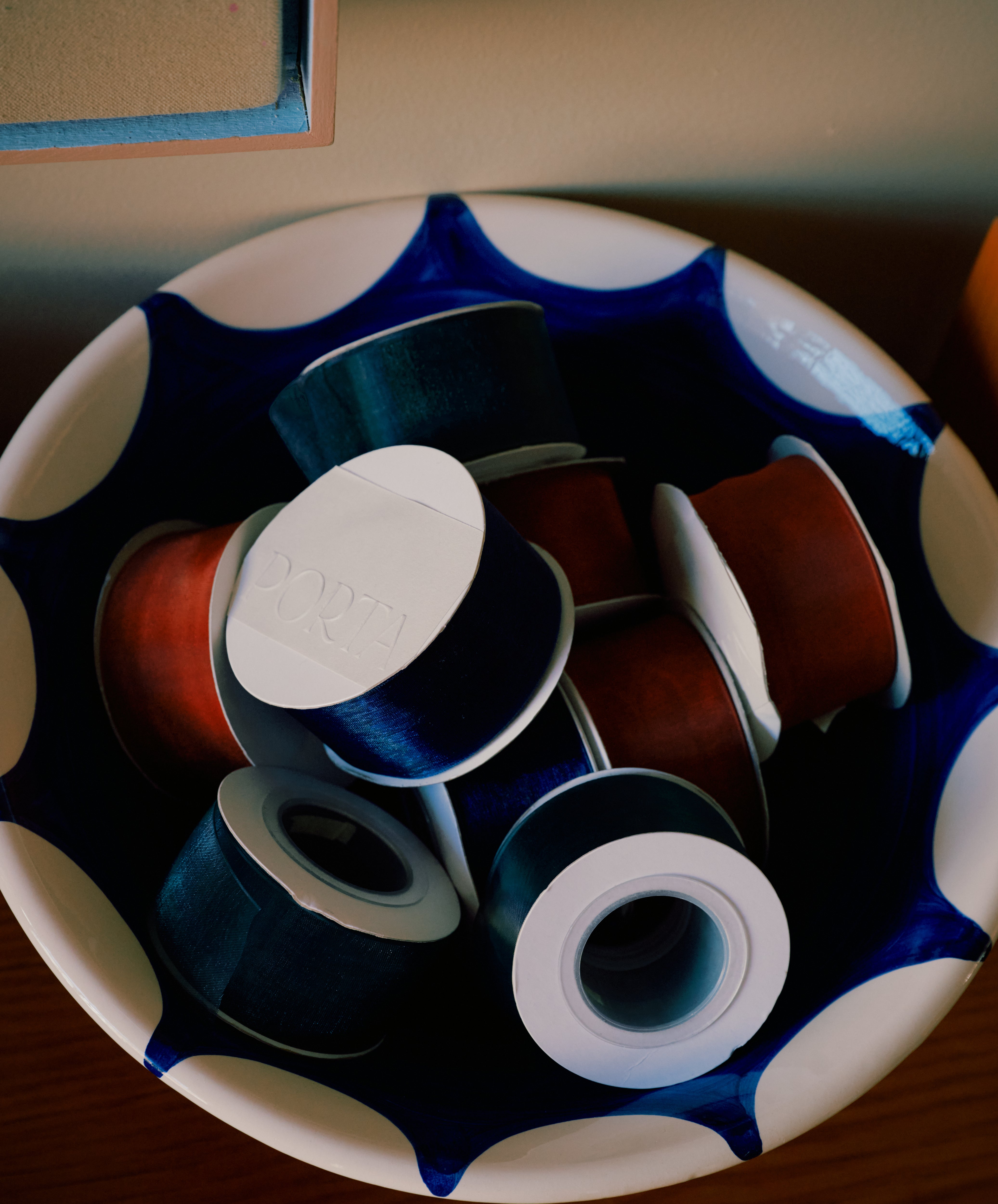 The Stella Serving Bowl, a handmade ceramic piece featuring a blue and white star-shaped design, is shown holding several black and reddish-brown spools of thread.