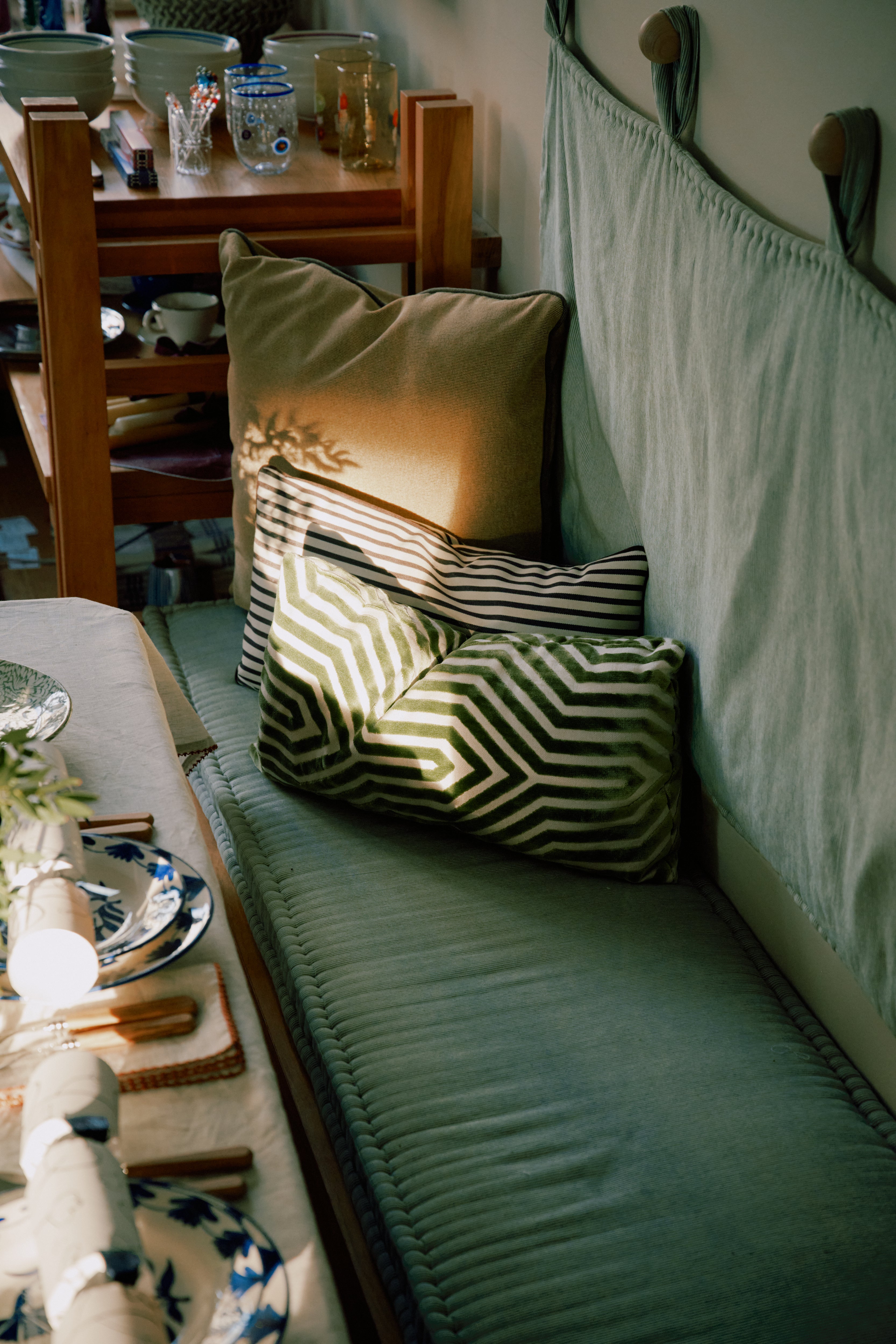 The Polo Lumbar Cushion, crafted from limited deadstock designer fabrics, adds comfort and style to a bench by the dining table as sunlight highlights its unique patterned design.