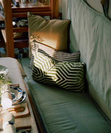 The Polo Lumbar Cushion, crafted from limited deadstock designer fabrics, adds comfort and style to a bench by the dining table as sunlight highlights its unique patterned design.