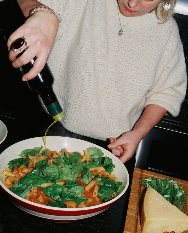 woman pouring oil over pasta dish