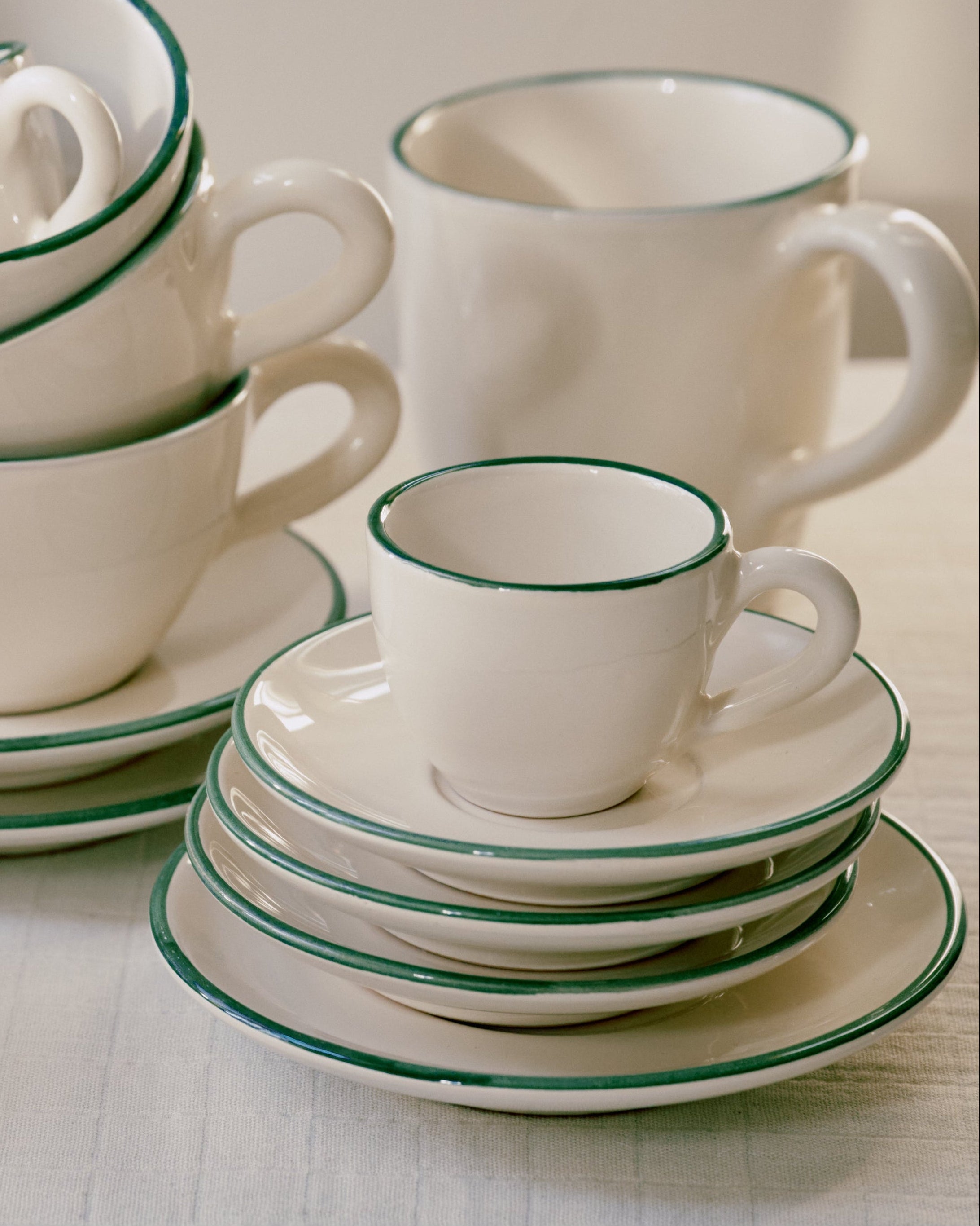 The Gio Espresso Set, featuring white ceramic cups and saucers with green rims, is neatly arranged on a table.