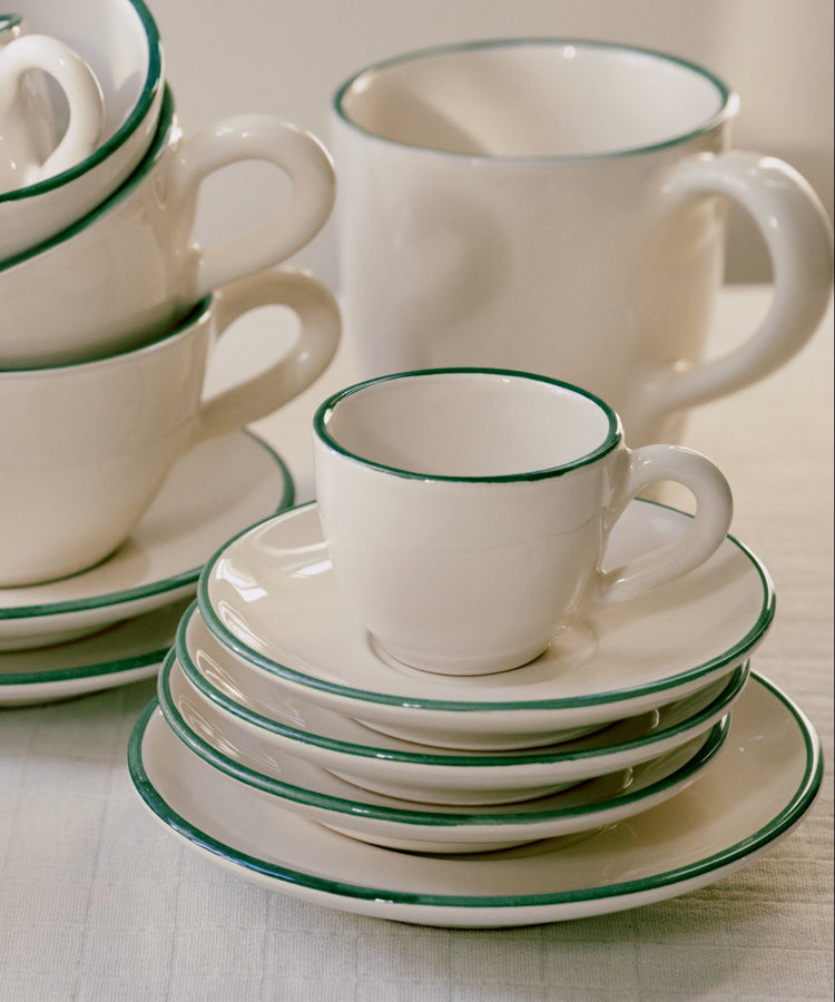 The Gio Espresso Set, featuring white ceramic cups and saucers with green rims, is neatly arranged on a table.
