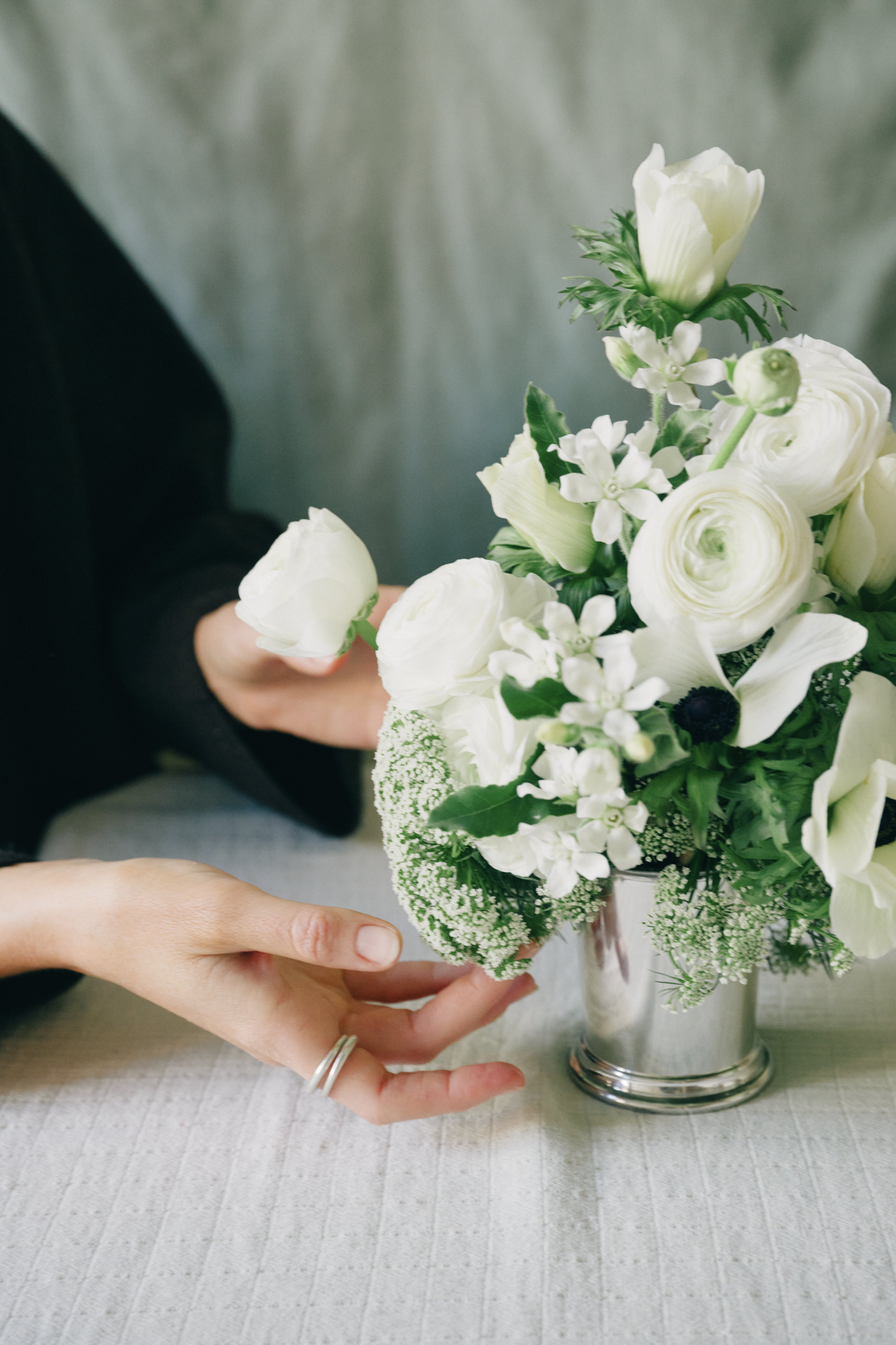 A person’s hand adjusts a small bouquet of white flowers arranged in the Clara Julep Cup on a light-colored surface.