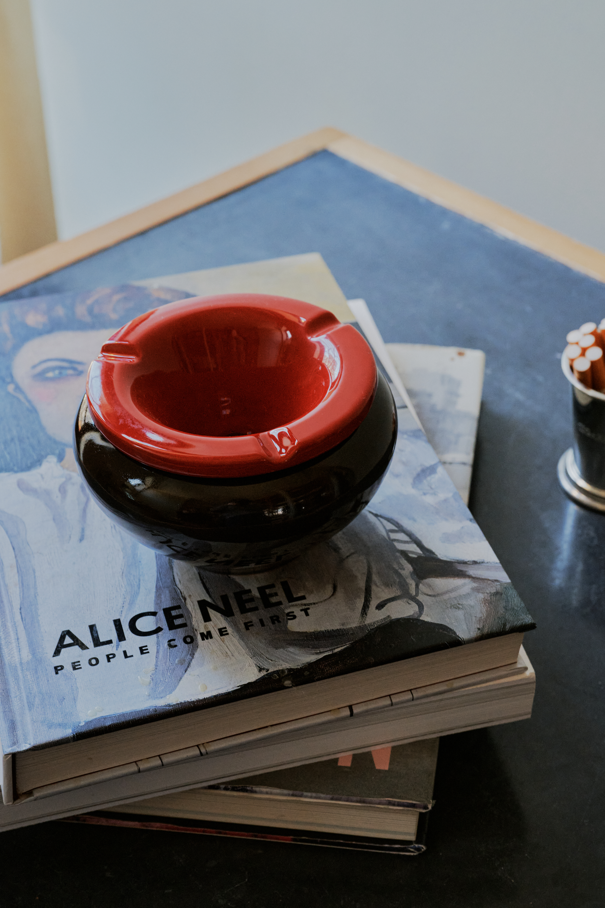 The Mix & Match Ashtray, a chunky ceramic piece handmade in Italy, sits on a dark tabletop atop a stack of books, the top titled Alice Neel: People Come First.