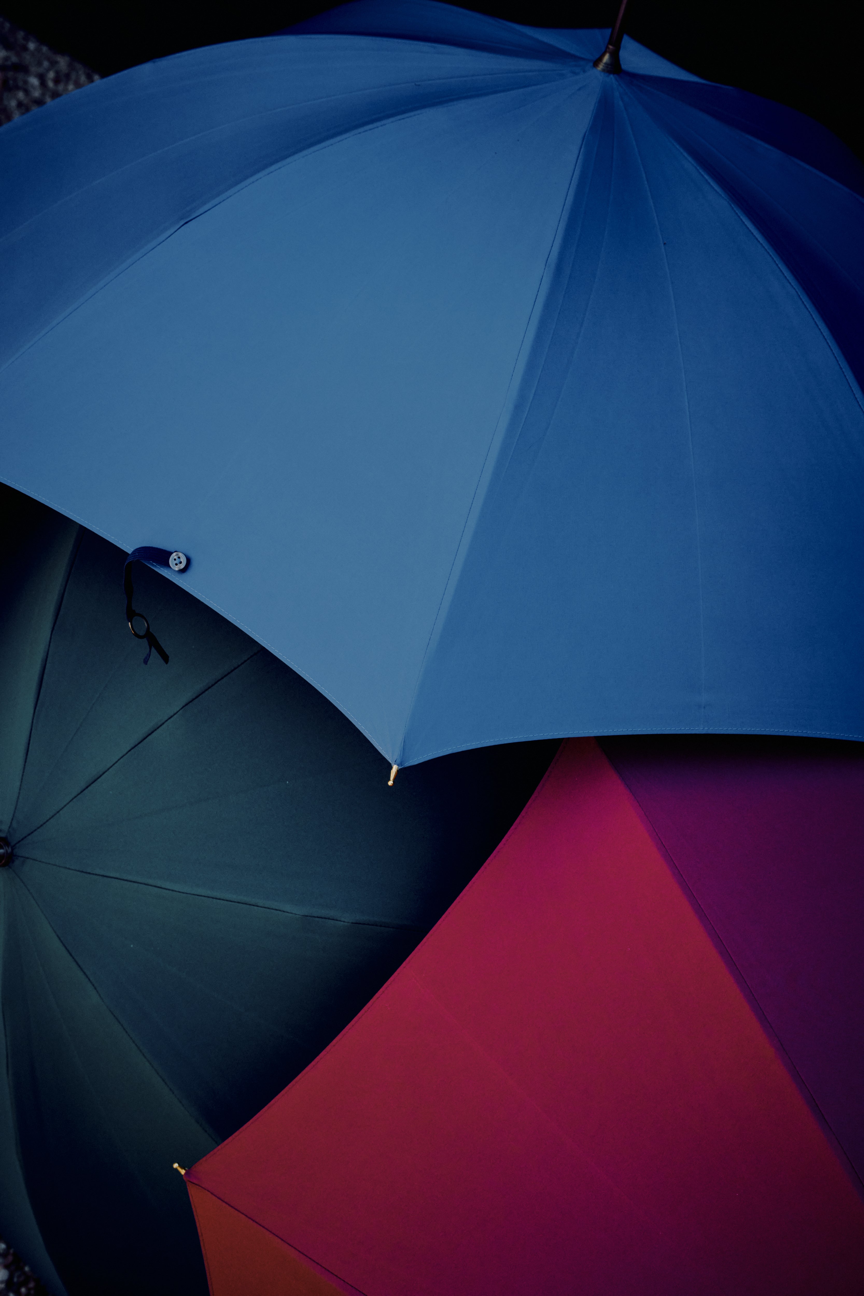 Three overlapping Victoria Ladies Umbrellas in blue, green, and red canopies are viewed from above against a dark background.