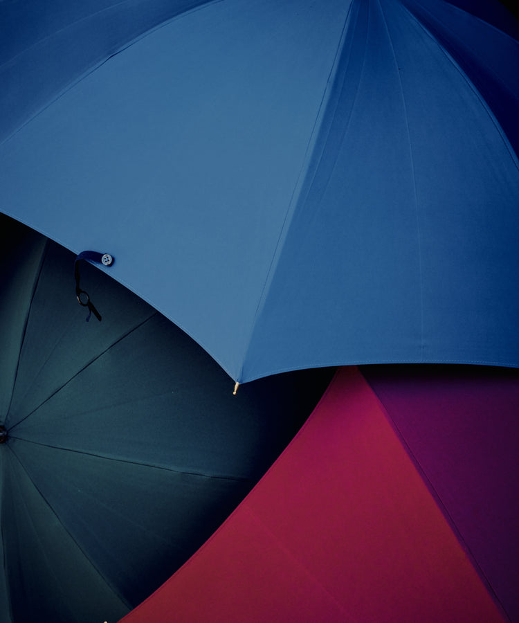 Three overlapping Victoria Ladies Umbrellas in blue, green, and red canopies are viewed from above against a dark background.