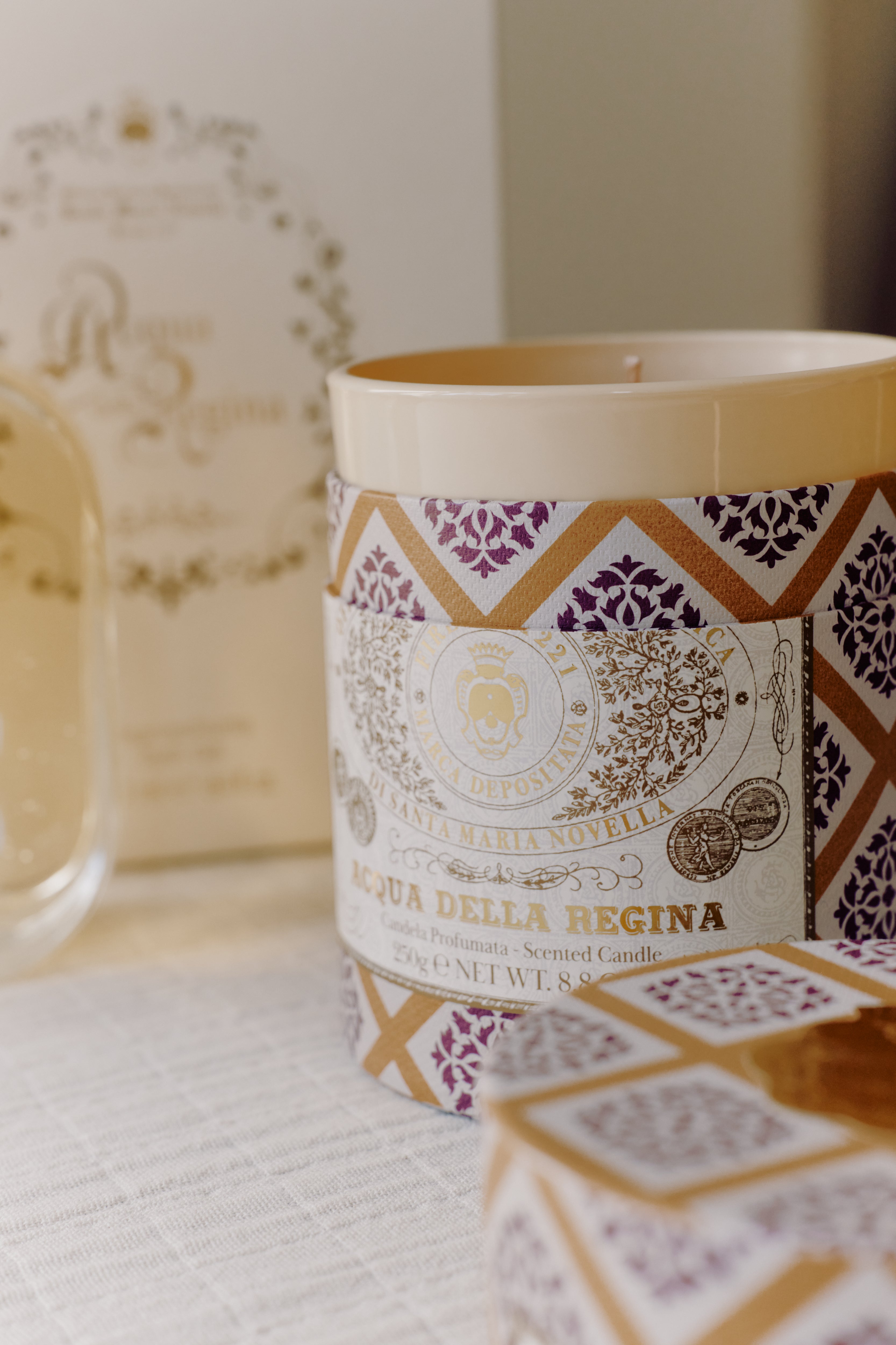 A close-up of the Acqua Della Regina Bundle, featuring a scented candle with a decorative label that highlights the iconic Florentine fragrance, displayed on a light surface.