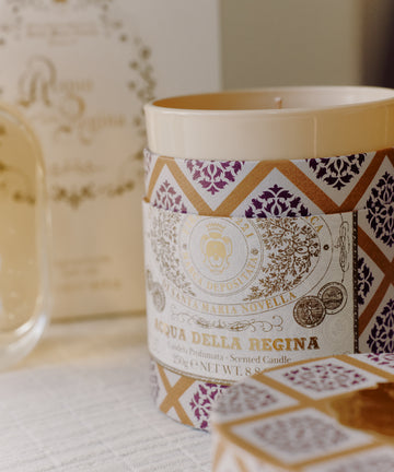 A close-up of the Acqua Della Regina Bundle, featuring a scented candle with a decorative label that highlights the iconic Florentine fragrance, displayed on a light surface.