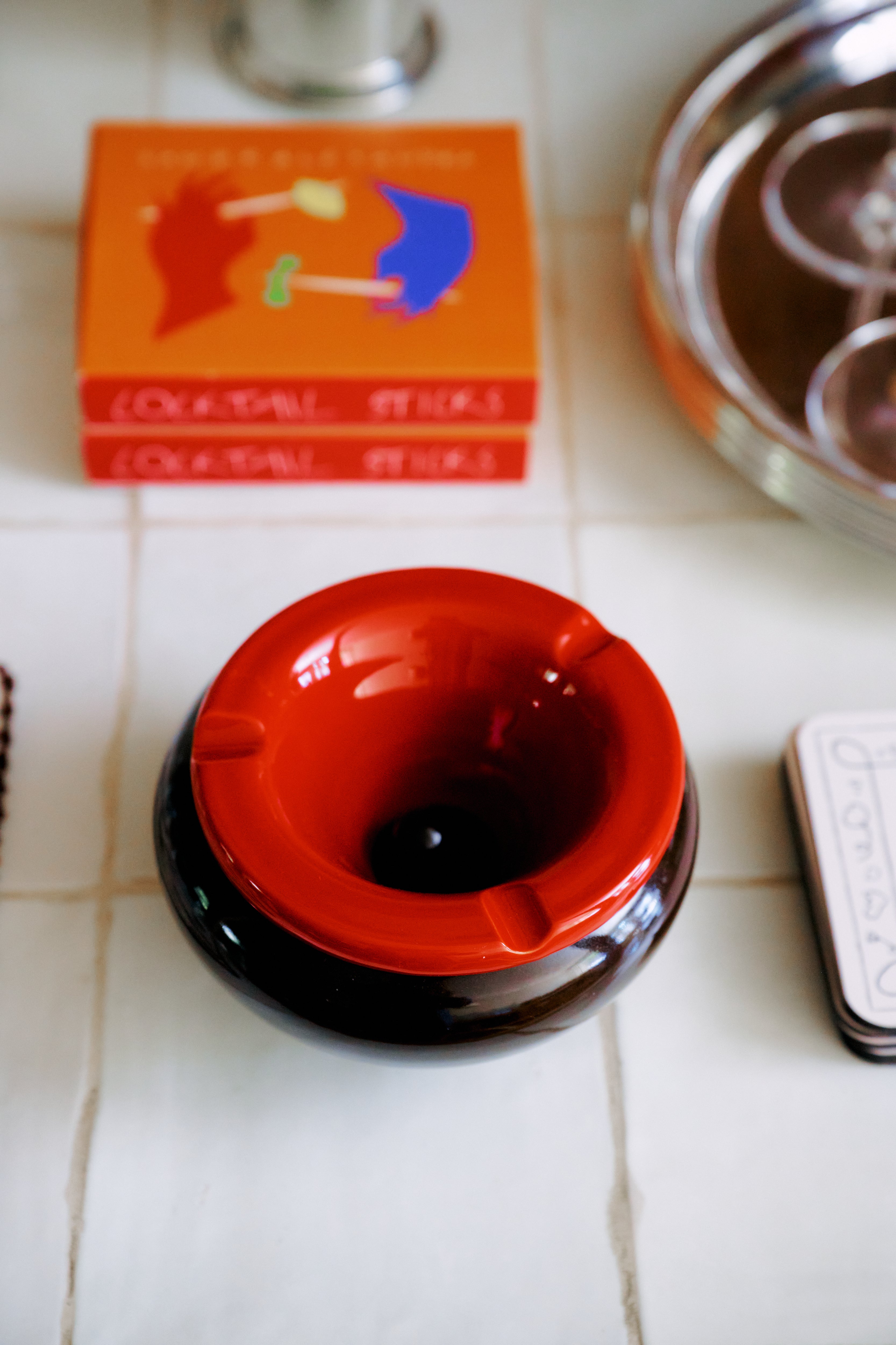 The Mix & Match Ashtray, a chunky ceramic piece handmade in Italy, rests on a tiled surface beside a stack of books and a silver tray.